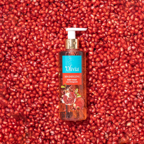 Bottle of Olivia skin energizing body wash surrounded by pomegranate seeds.