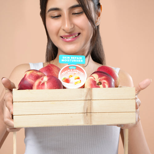 A young woman holding a wooden crate filled with red peaches and a yogurt container.