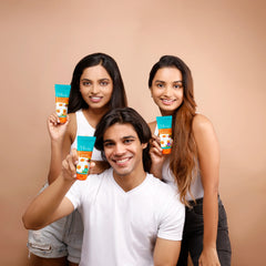 Three young Indian models smiling and holding Olivia Ultra Protect+ Sunscreen tubes in SPF 40 and SPF 50 variants with chamomile extract against a beige studio background